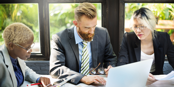 Three people gather around a laptop.